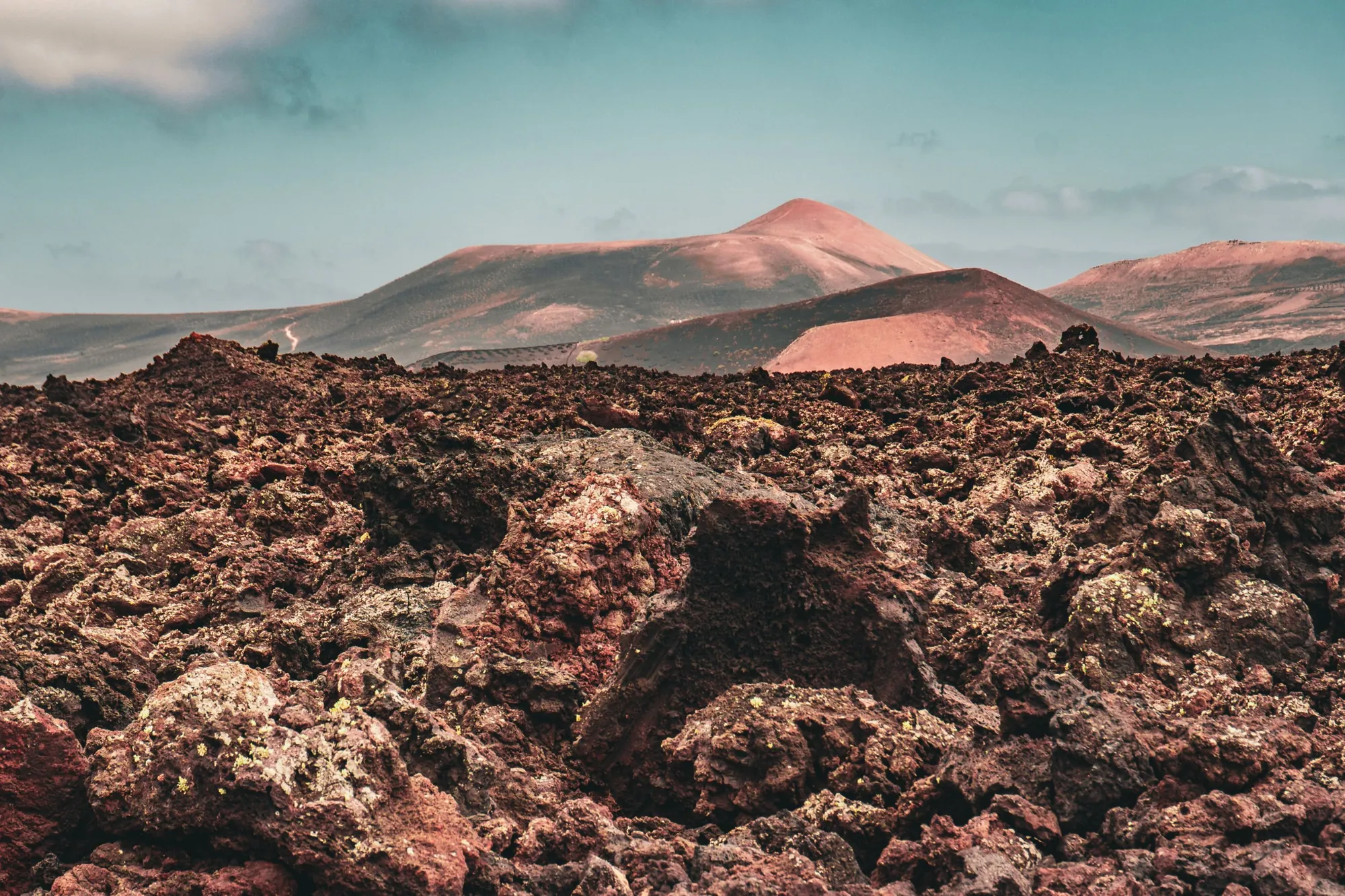 Rough red lava rock in front of rust-coloured volcanic cones