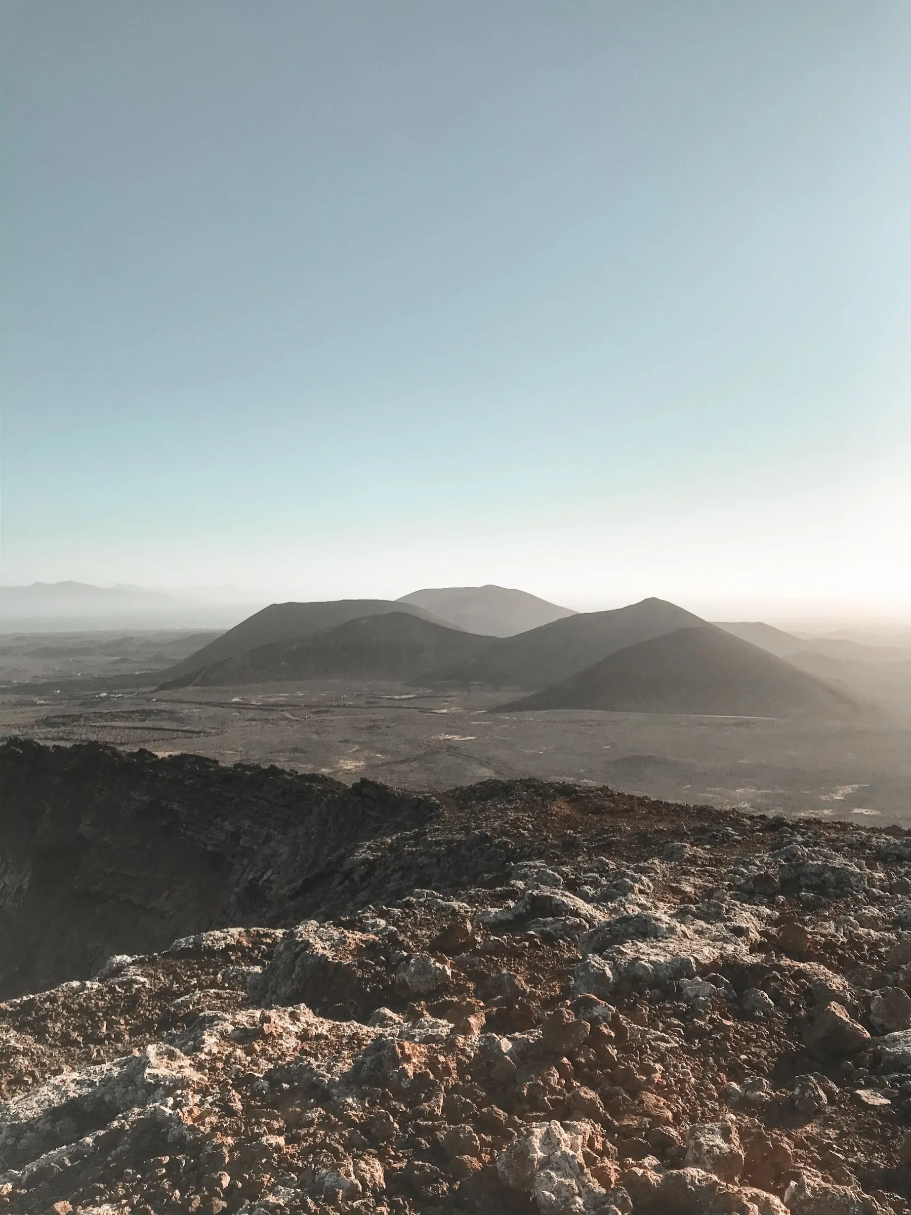 A row of dark volcanic cones in soft haze, seen from the rocky rim of a crater